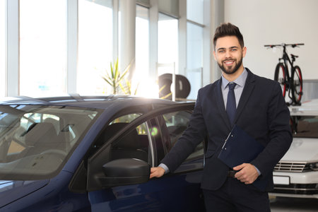 Young salesman with clipboard near car in dealershipの写真素材