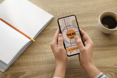 Woman ordering taxi with smartphone at wooden table, closeupの写真素材