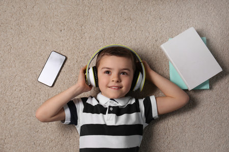 Cute little boy listening to audiobook on floor, top view