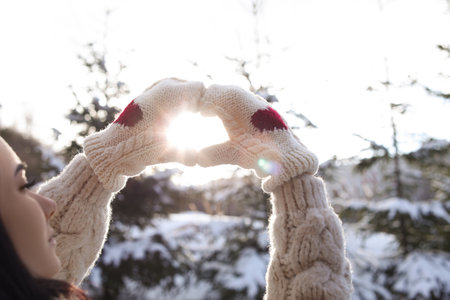 Young woman making heart with hands outdoors, closeup. winter holidays