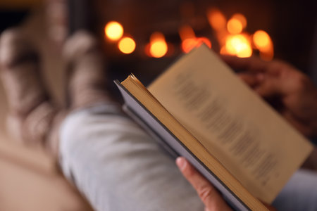 Man reading book near fireplace at home, closeupの写真素材