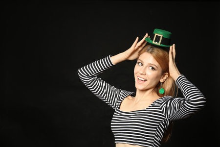 Young woman with green leprechaun hat on black background, space for text. St. Patrick's Day celebrationの写真素材