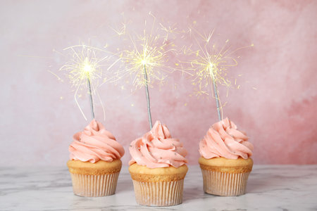 Birthday cupcakes with sparklers on table against light pink backgroundの写真素材