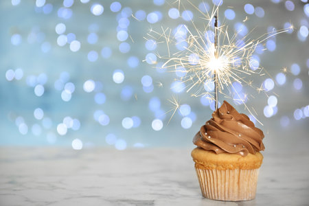 Birthday cupcake with sparkler on table against blurred lights. Space for textの写真素材