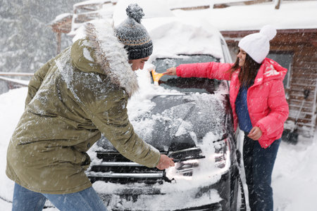 Young couple cleaning snow from car outdoors on winter dayの写真素材
