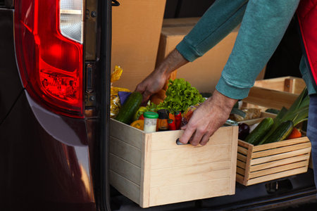 Courier taking crate with products from car, closeup. food delivery service