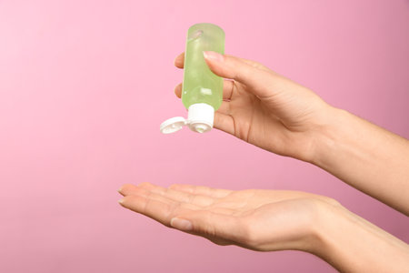 Woman applying antiseptic gel on pink background, closeupの写真素材