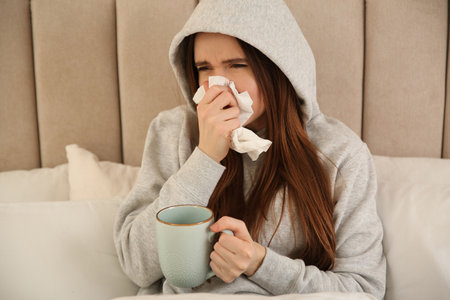 Sick young woman with cup of hot drink in bed at home. Influenza virusの写真素材
