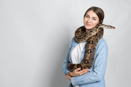 Young woman with boa constrictor on light background, space for text. exotic petの写真素材