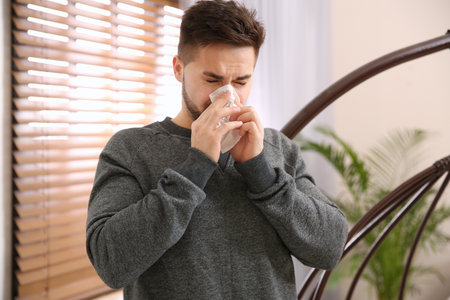 Sick young man sneezing at home. Influenza virusの写真素材