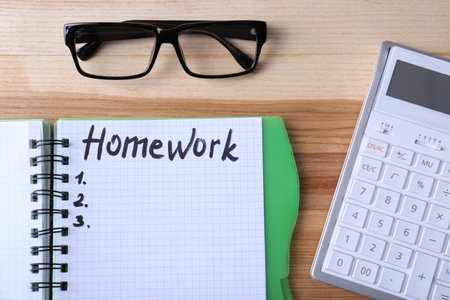 Word HOMEWORK in notebook, glasses and calculator on wooden table, flat layの写真素材