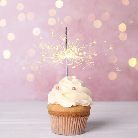 Birthday cupcake with sparkler on white wooden table against light pink backgroundの写真素材