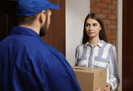 Young woman receiving parcel from delivery man indoorsの写真素材
