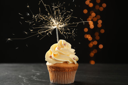Birthday cupcake with sparkler on table against dark backgroundの写真素材