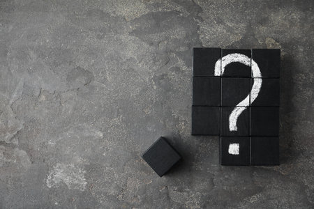 Black wooden cubes with question mark on gray stone table, flat lay. Space for text