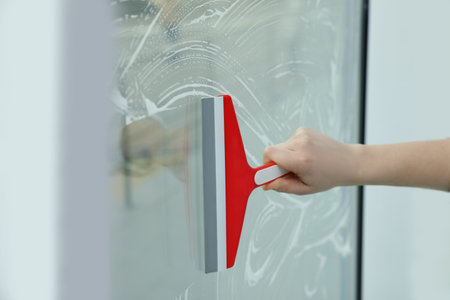 Woman cleaning window with squeegee indoors, closeup