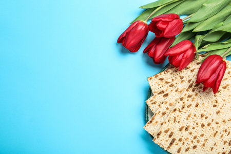 Matzos and flowers on light blue background, flat lay with space for text. Passover (Pesach)