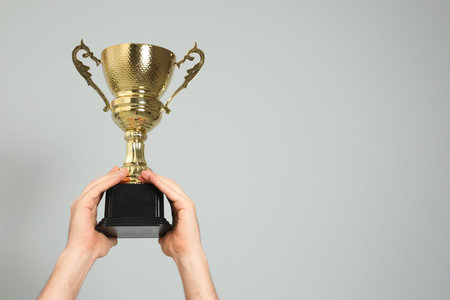 Man holding gold trophy cup on light gray background, closeup. Space for textの写真素材