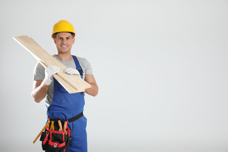 Handsome carpenter with wooden planks on light background. Space for text