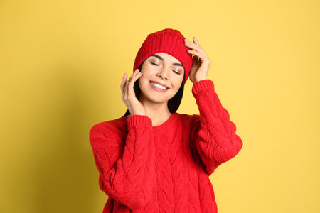 Young woman wearing warm sweater and hat on yellow background. winter seasonの写真素材