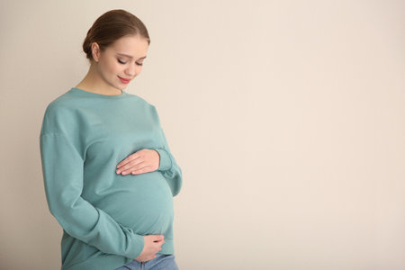 Young pregnant woman on beige background. Space for text