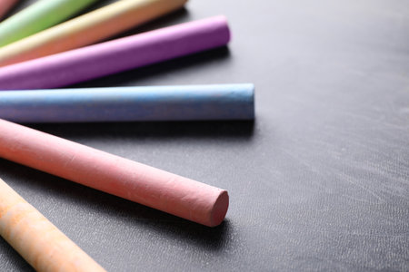 Pieces of color chalk on blackboard, closeup. Space for text