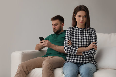 Young man preferring smartphone over his girlfriend at home. relationship problemsの写真素材