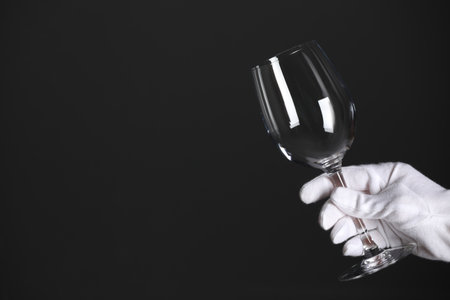 Person in white glove checking cleanliness of glass on dark background, closeup. Space for text