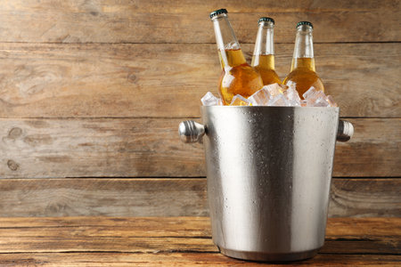Metal bucket with beer and ice cubes on wooden background. Space for textの写真素材