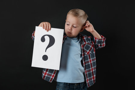 Confused boy holding sheet of paper with question mark on black background