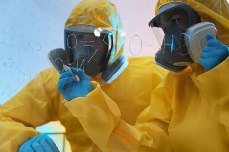 Scientists in chemical protective suits writing formula on glass board at laboratory. virus researchの写真素材