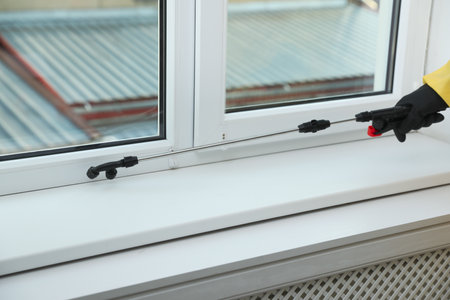 Pest control worker in protective suit spraying insecticide on window sill indoors, closeupの写真素材