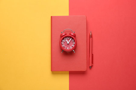 Red notebook, alarm clock and pen on color background, top viewの写真素材