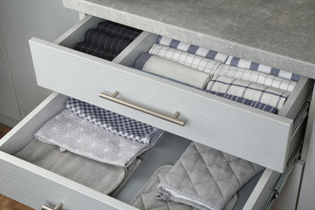 Open drawers with folded towels and oven mittens. Order in kitchenの写真素材