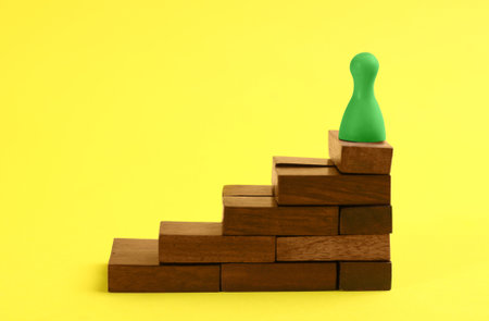 Green game piece on top of stairs against yellow background. career promotion concept