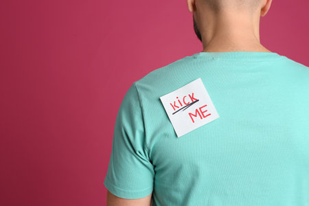 Man with KICK ME sticker on back against pink background, space for text. April fool's dayの写真素材