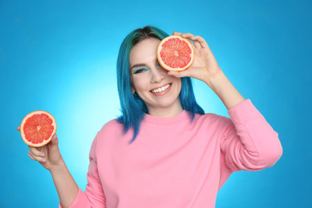 Young woman with bright dyed hair holding grapefruit on light blue backgroundの写真素材