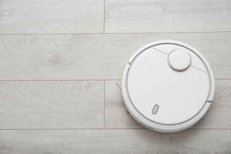 Modern robotic vacuum cleaner on wooden floor, top view. Space for textの写真素材
