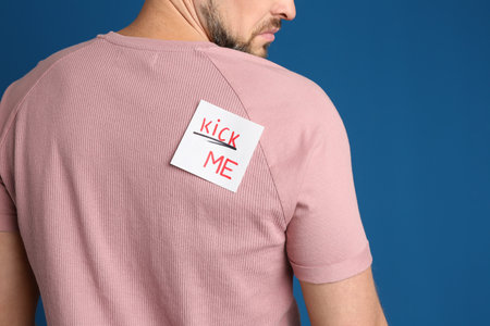 Man with KICK ME sticker on back against blue background, closeup. April fool's dayの写真素材