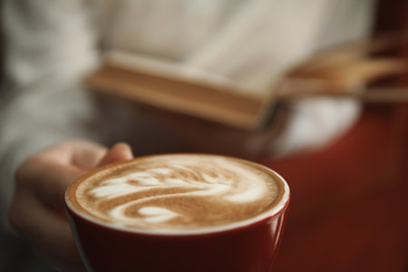 Woman with coffee reading book indoors, focus on cupの写真素材