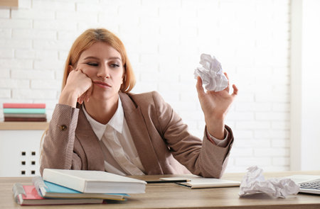 Lazy employee playing with crumpled paper at table in officeの写真素材