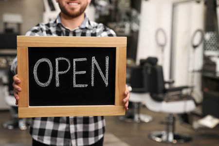Young business owner holding OPEN sign in his barber shop, closeup