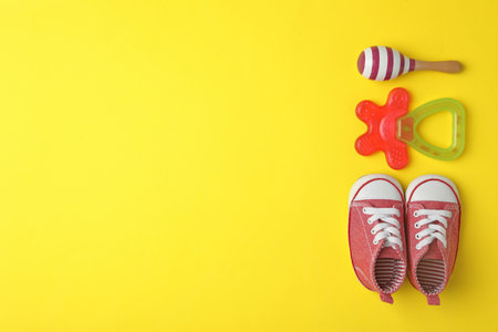 Child's shoes, toy and teether on yellow background, flat lay with space for textの写真素材