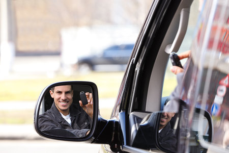Man with key looking into side view mirror of modern car outdoors. Buying new cars