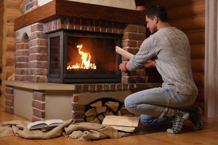 Man putting dry firewood into fireplace at home. winter holidaysの写真素材