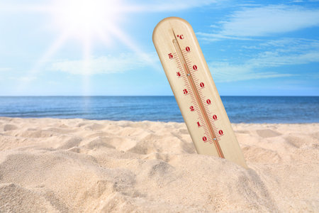 Weather thermometer with high temperature on sandy beach near sea