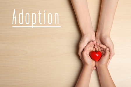 Woman and child holding heart on beige wooden background, top view. Adoption conceptの写真素材