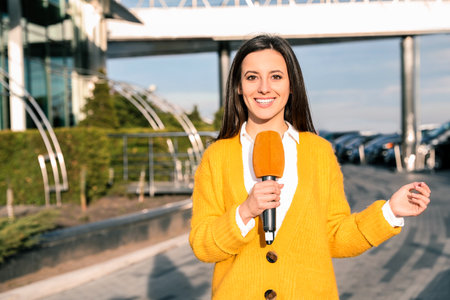 Young female journalist with microphone working on city streetの写真素材