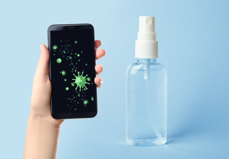 Sanitizing mobile devices during virus outbreak. Antiseptic spray and woman with smartphone on blue background, closeupの写真素材