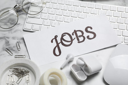 Card with word JOBS, computer keyboard, earphones and stationery on white marble table. career conceptの写真素材